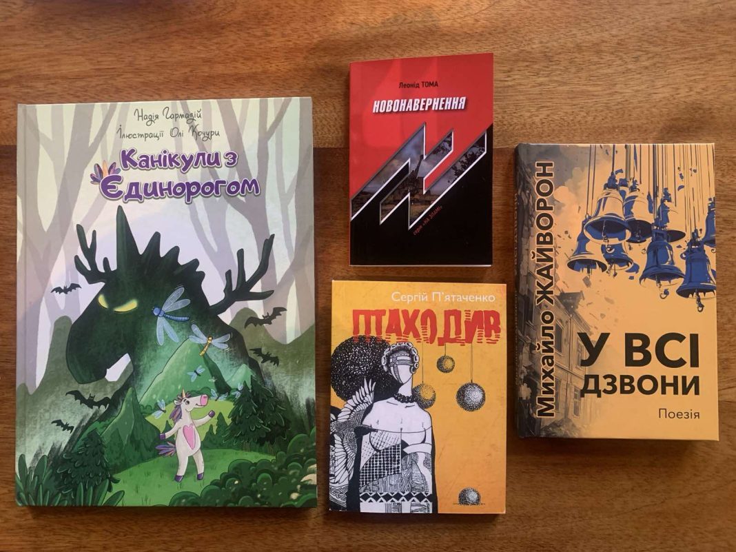 Чотири книги. 1. Ліва книга: "Канікули з Єдинорогом" Надії Гербіш з ілюстраціями Олі Кузьмін. На обкладинці зображені єдиноріг і дракон у лісі. 2. Верхня права книга: "Новонавернення" Леоніда Томи з чорно-червоним дизайном. 3. Нижня права книга: "Пахощі" Сергія П’ятаченка з зображенням композиції, що складається із жіночого силуету і декоративних елементів. 4. Права книга: "У всі дзвони" Михайла Жайворона, яка є поетичною збіркою. На обкладинці зображені дзвони. Книги розташовані на дерев'яній поверхні.